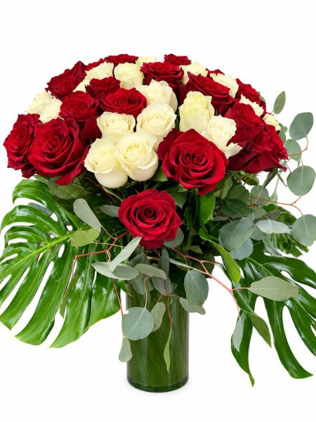 Red and white rose luxury bouquet with monstera leaves and eucalyptus in a green glass vase