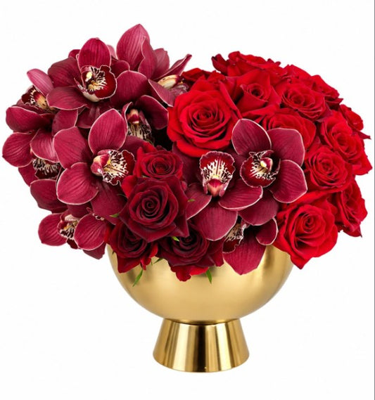 Red roses and burgundy cymbidium orchids arranged in a gold bowl vase